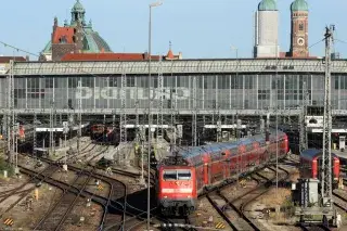 Eine rote Lok mit einem Regionalexpress fährt auf den Gleisen aus der Haupthalle des Münchner Hauptbahnhofs