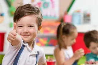 Ein Kind spielt in der Kinderbetreuung und zeigt den Daumen nach oben