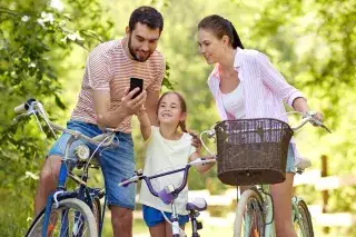 Vater, Mutter und Kind stehen mit ihrem Fahrrad und schauen auf ein Smartphone