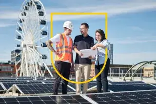 Drei Personen planen ein Bauvorhaben auf einem Dach mit Solaranlage