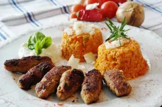 A plate with six cevapcici meat rolls and rice