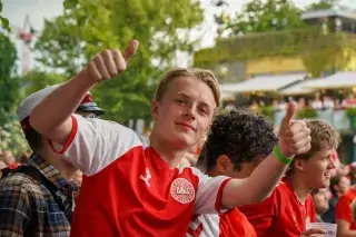 A young, blond football fan with a Denmark jersey points both thumbs up