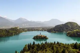 Panorama des Sees Bled in Slowenien mit kristallklarem Wasser bei blauem Himmel und Wäldern am Ufer