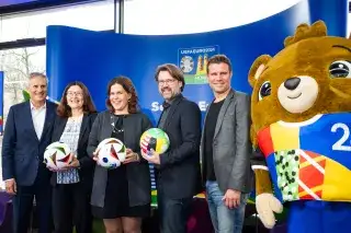 Fünf Personen und Maskottchen Albärt posieren beim Presse-Event zu „100 days to go“ vor der UEFA EURO 2024 in der Host City München für die Kamera