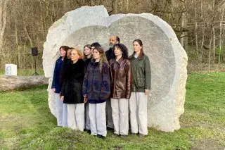 Ein Chor steht vor einem Klangkunstwerk, das aus einem großen Stein geschliffen wurde