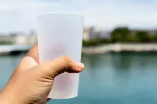 Hand hält Mehrwegbecher vor einem See